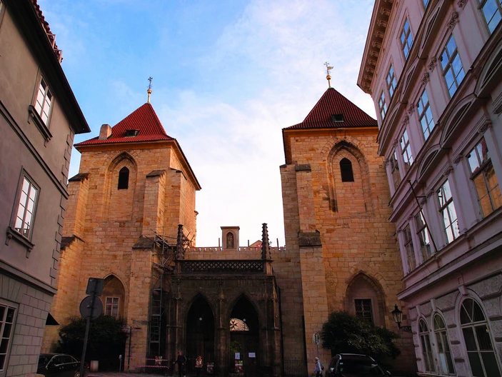 Dos altas torres de piedra con tejados rojos y puertas arqueadas, flanqueadas por edificios con ventanas