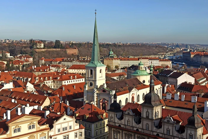 vista panorámica de Praga con tejados rojos, una aguja verde y un río