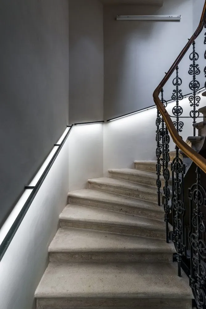 escalera de piedra con barandilla de metal ornamentada e iluminación de pared