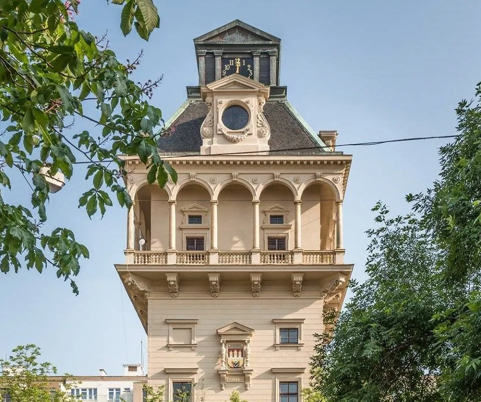La Torre de Agua de Letná con arquitectura ornamentada, ventanas arqueadas y una esfera de reloj, rodeada de árboles.