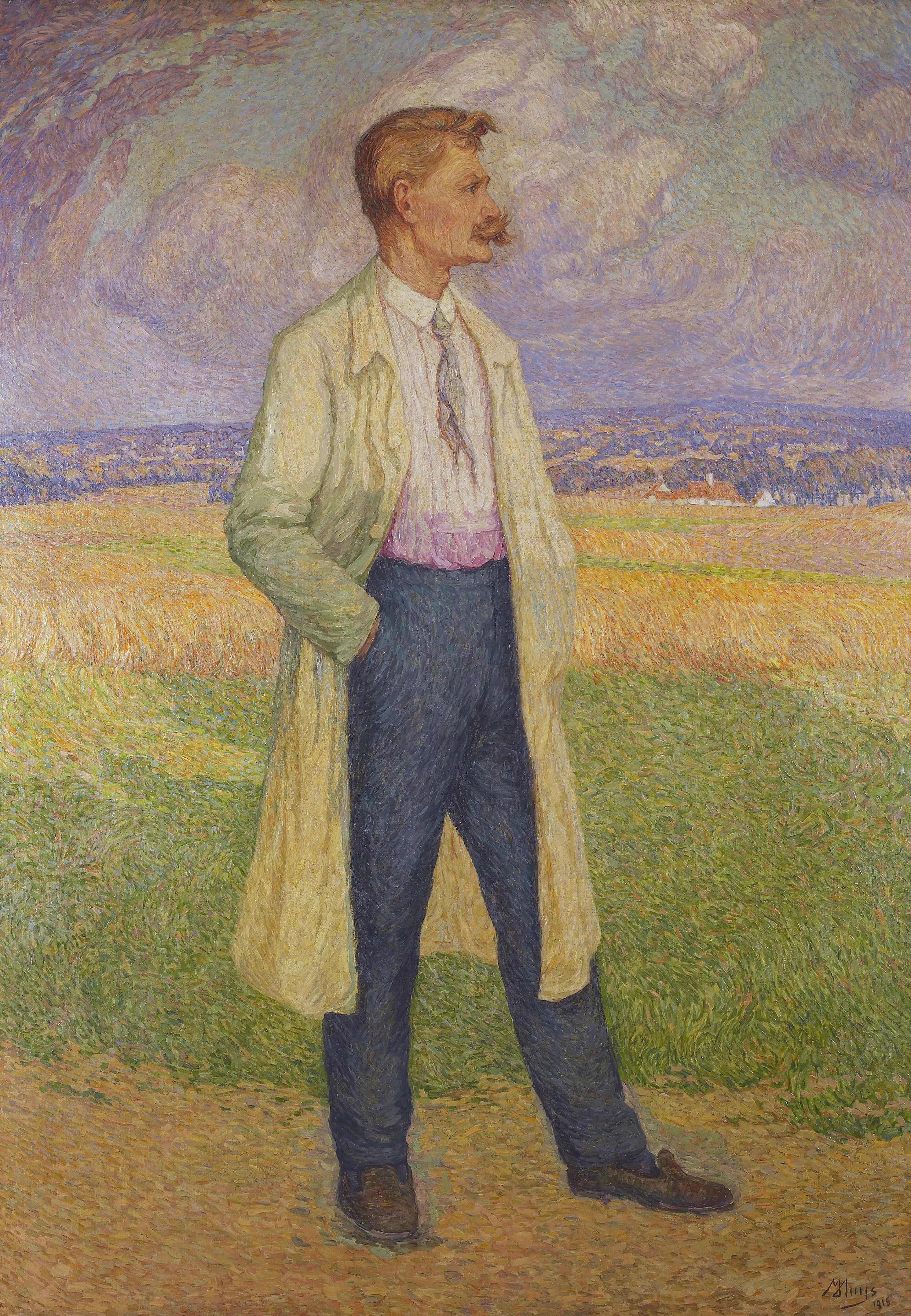 Retrato de un hombre con bigote de pie en un campo, vistiendo un abrigo largo de color claro y pantalones oscuros bajo un cielo nublado.