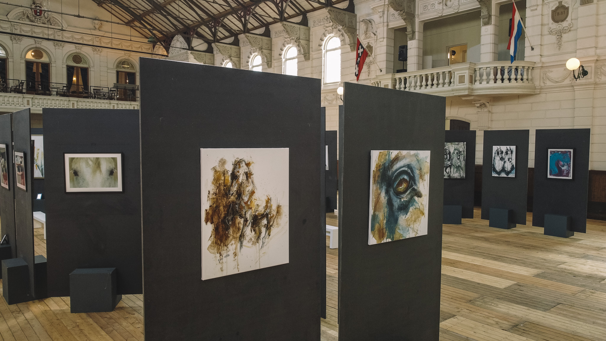 Museum tentoonstellingshal met zwarte vitrinepanelen waarop paardenthema-kunstwerken worden getoond in een groot historisch gebouw met hoge plafonds