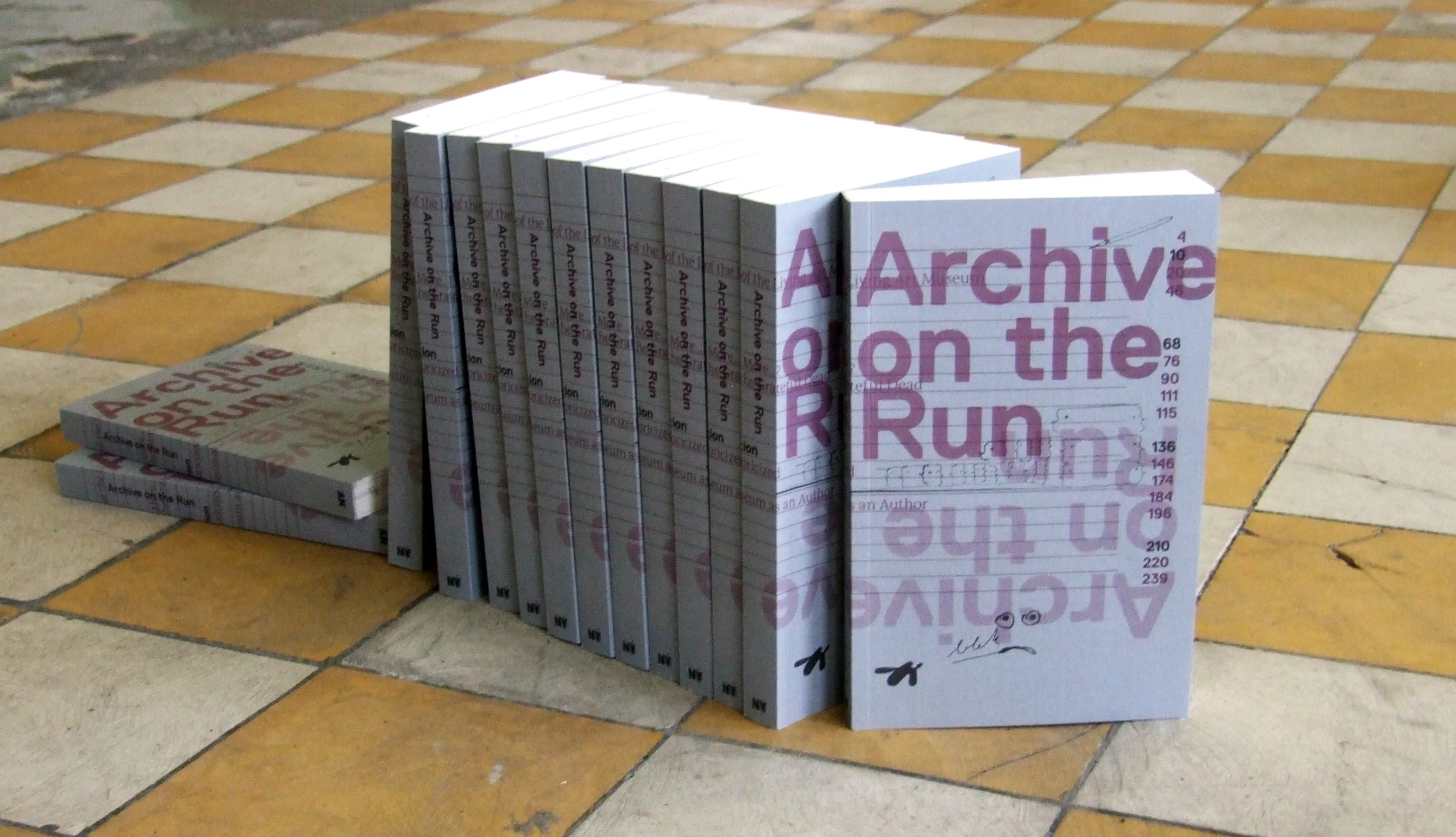 Stapel witte boeken getiteld 'Archive on the Run' gerangschikt op een beige en crèmekleurige geblokte tegelvloer