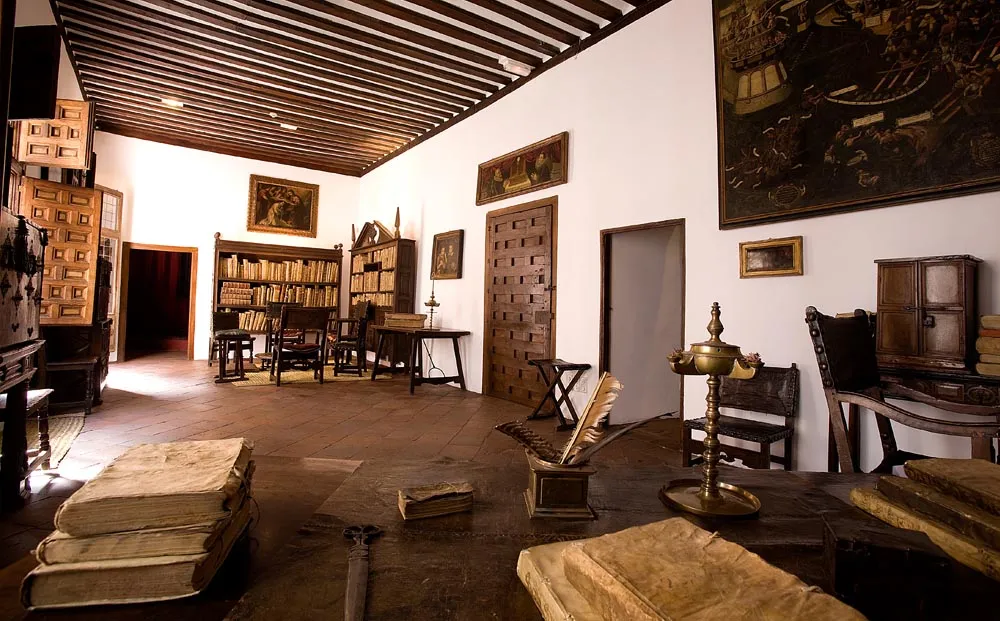 Interior of a historic room with wooden beams, bookshelves, and antique furniture