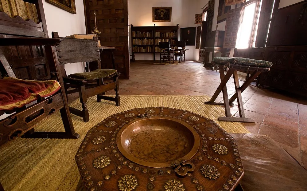 wooden table with ornate bowl, chairs, and bookshelf in a historic room