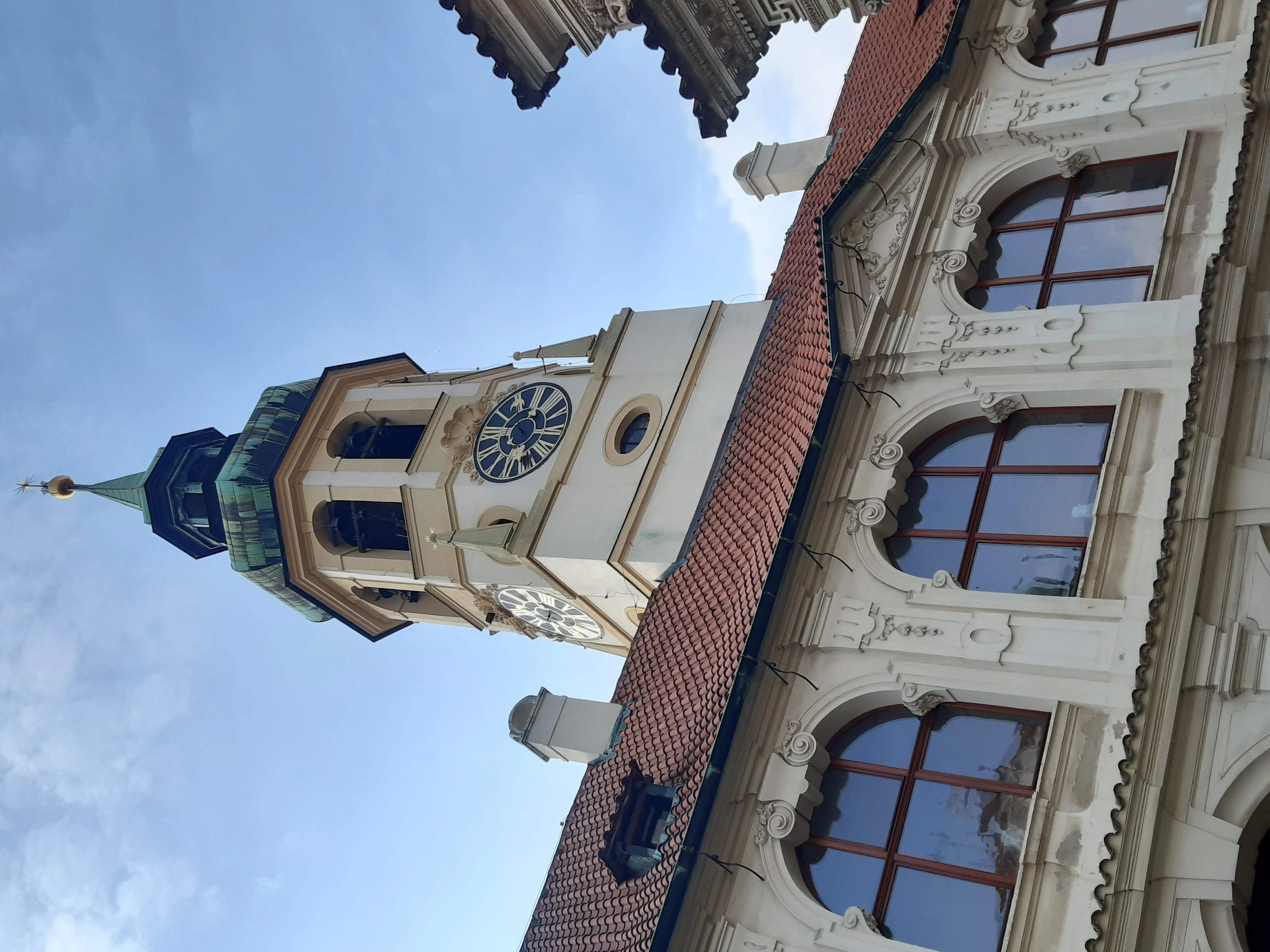 Barok gebouw met een klokkentoren en rood pannendak onder een blauwe lucht