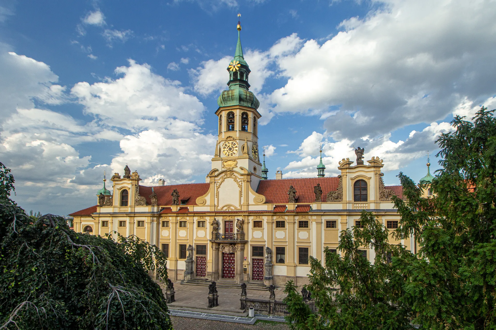 Barokowy budynek z zieloną iglicą i wieżą zegarową pod błękitnym niebem z chmurami