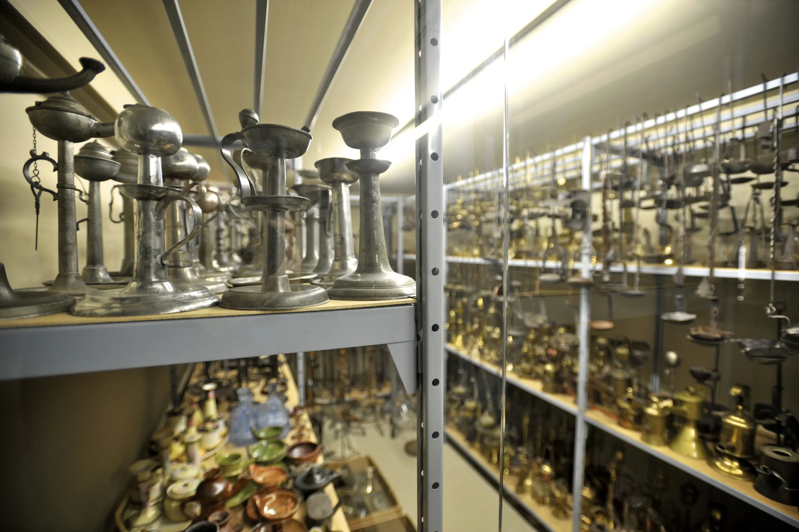 Estanterías metálicas llenas de filas de candelabros, lámparas de aceite y diversos objetos de iluminación dentro de un museo