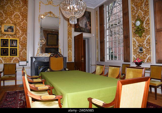Elegant historic room with green tablecloth, wooden chairs, ornate yellow wallpaper, crystal chandelier, and large windows