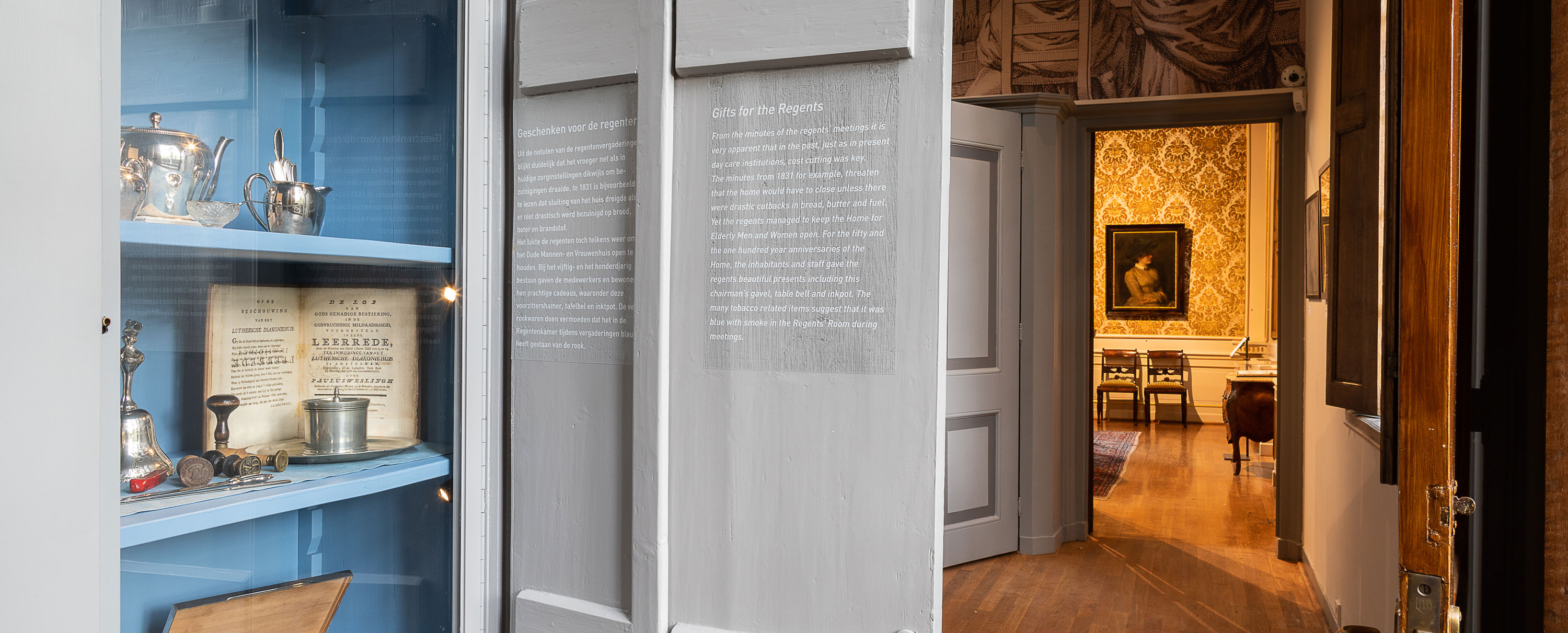 Vista interior del Museo Lutero que muestra una vitrina azul con artefactos históricos y una puerta que conduce a una habitación con un cuadro enmarcado y sillas de madera.