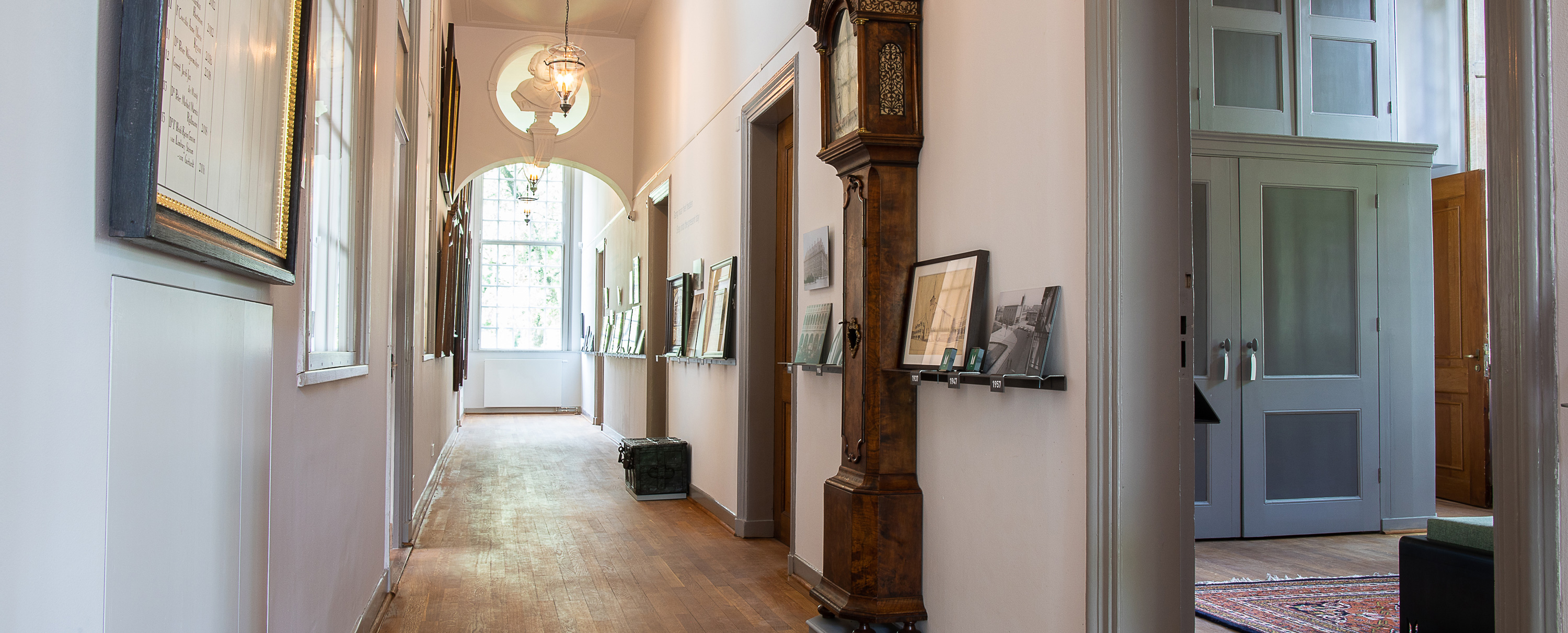Long hallway inside Luther Museum with framed exhibits on white walls, tall wooden clock, and sunlit entrance at the far end