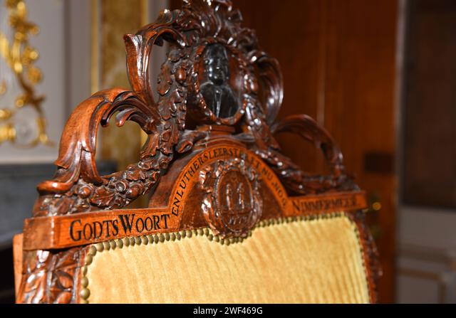 Ornato tallado silla de madera con inscripción 'GODTS WOORT' y intrincados elementos decorativos, probablemente parte de una exposición histórica luterana