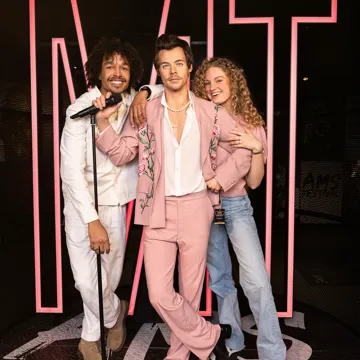 Three wax figures in pink and white outfits posing in front of a pink 'MT' Madame Tussauds Amsterdam backdrop.