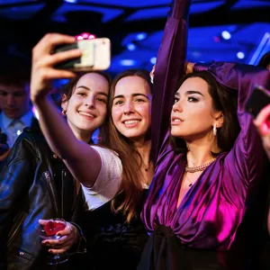 Drie mensen die een selfie maken met een levensechte wassen figuur in een paarse jurk bij een museumexpositie