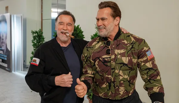 Arnold Schwarzenegger standing next to a wax figure of himself in a camouflage jacket