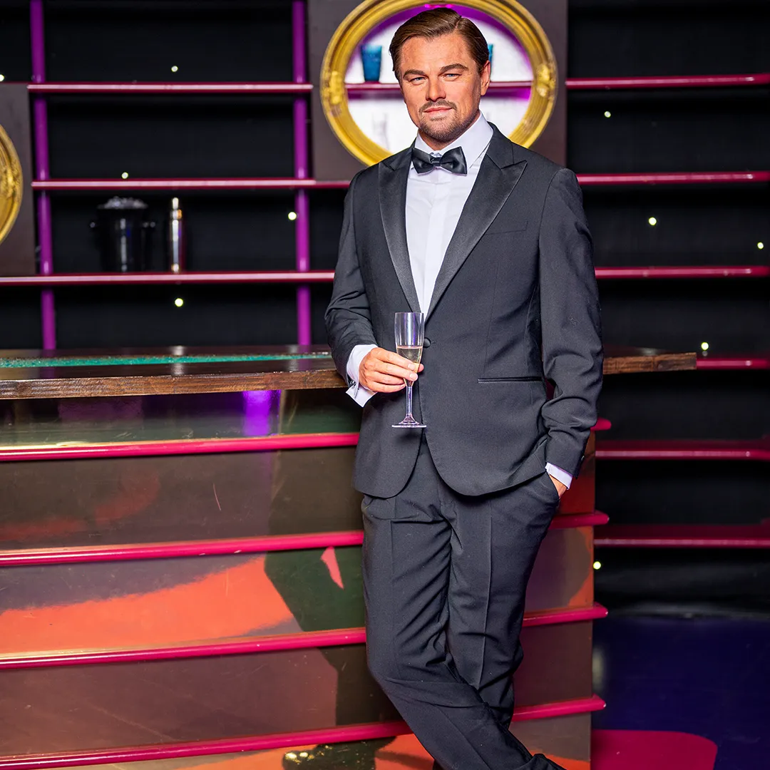 wax figure of a man in a black tuxedo holding a glass