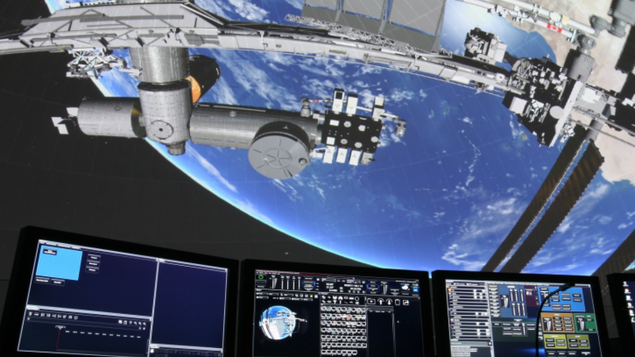 A large dome screen showing a space station orbiting Earth, with control panels in the foreground