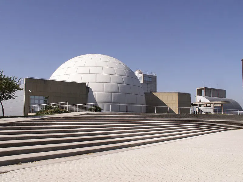 Silver dome of the Madrid Planetarium with concrete steps and modern buildings under a clear blue sky