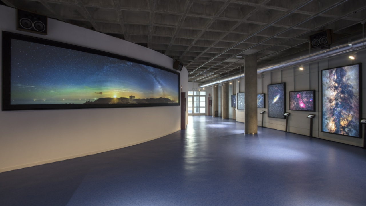 long hallway in a museum with large curved screens displaying space scenes