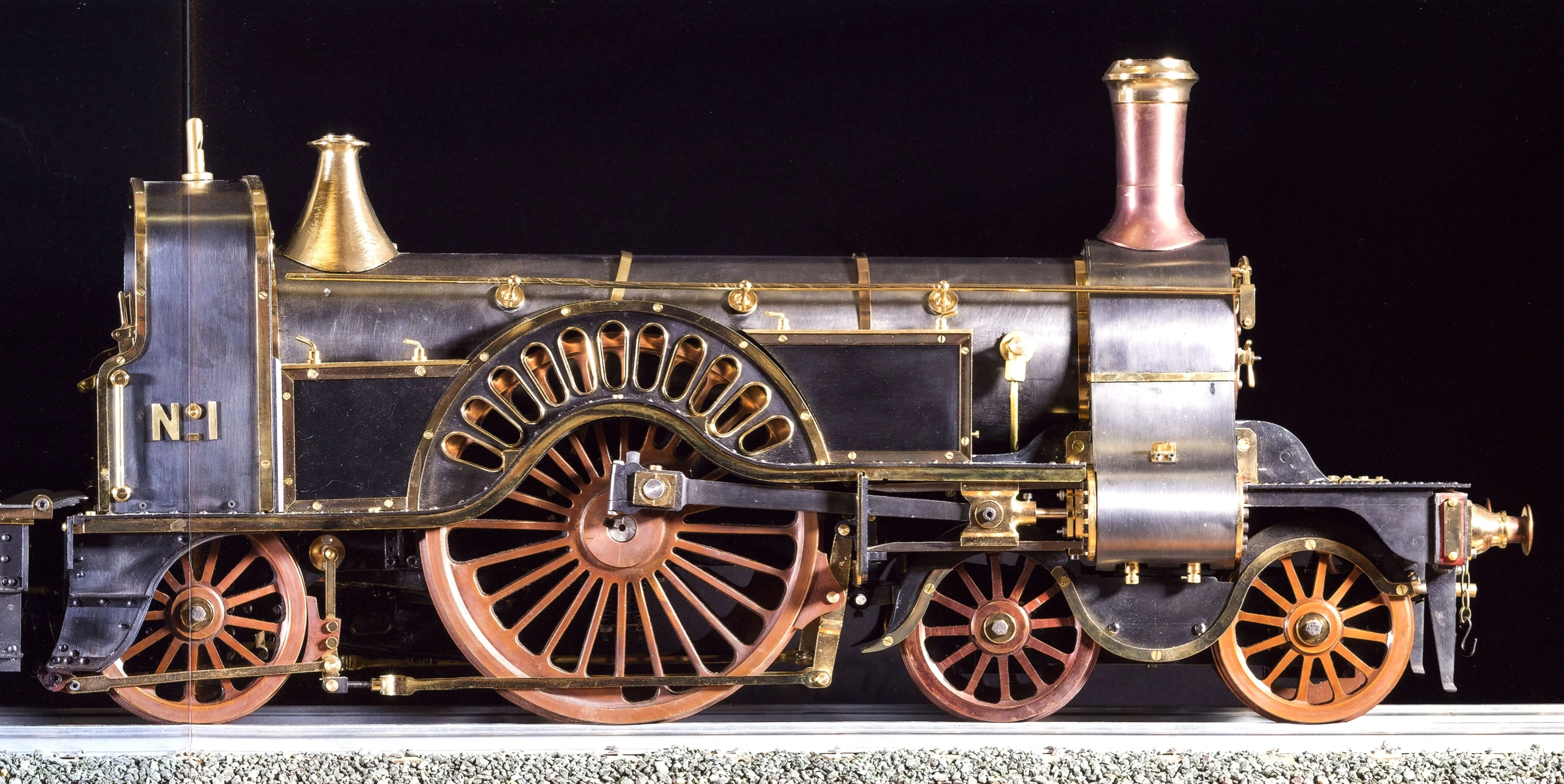 A detailed model of a steam locomotive with brass and metal accents, large spoked wheels, and a black and gold finish, displayed on a track.