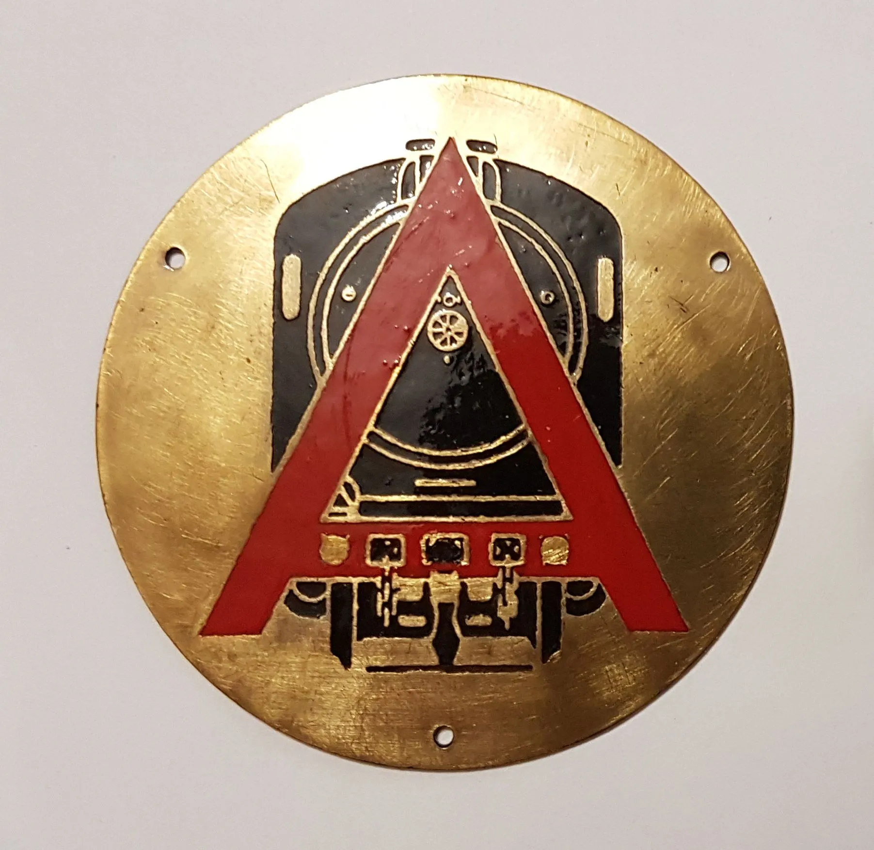 Circular brass plaque with a black steam locomotive and red triangle design