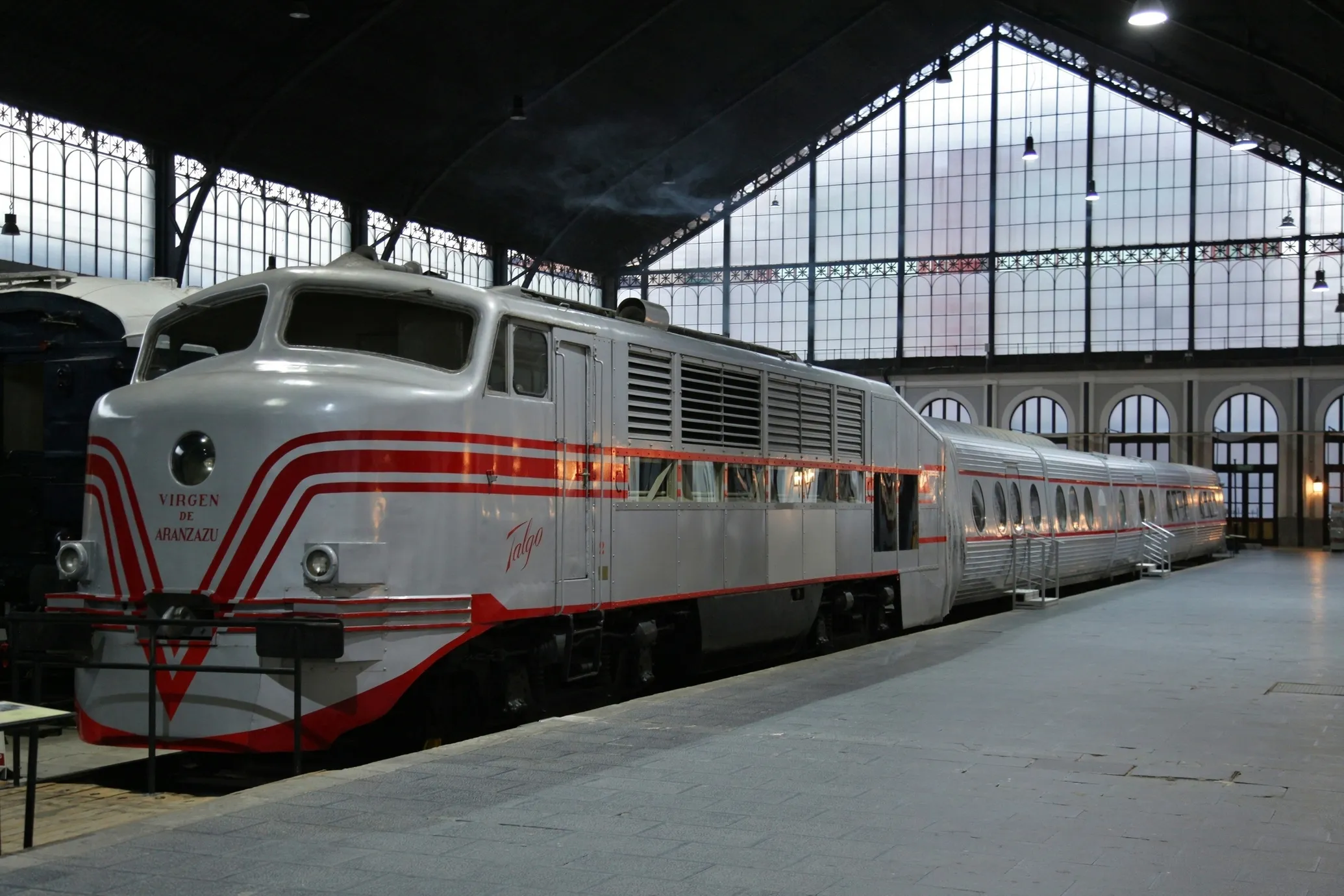 A silver and red vintage train on display inside a large hall with a high glass ceiling