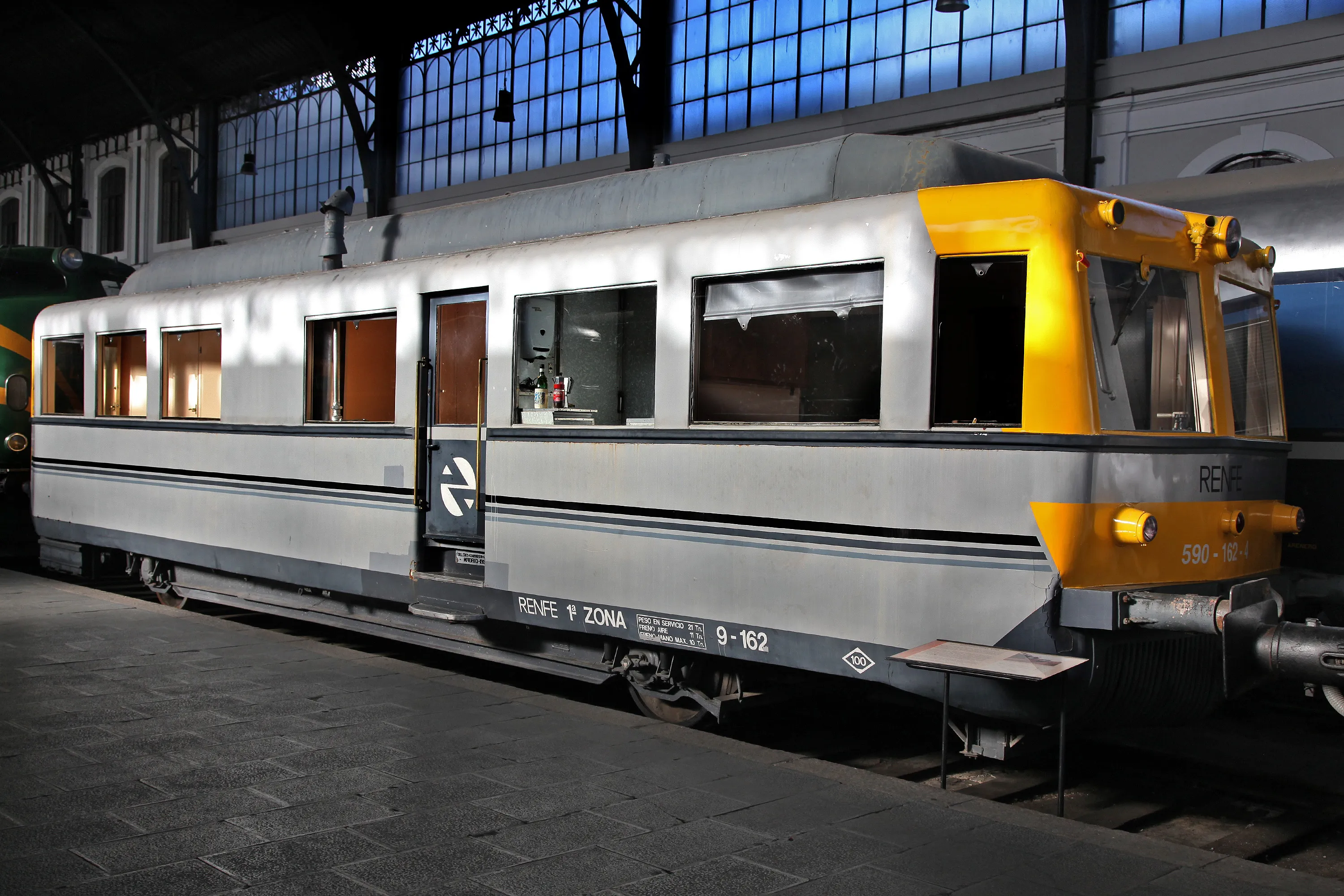 A silver and yellow train car on display inside a museum with large arched windows