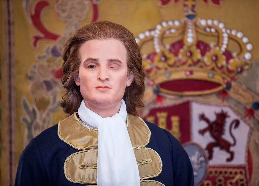 figura de cera de un hombre con ropa histórica, con una corona y un escudo de armas detrás