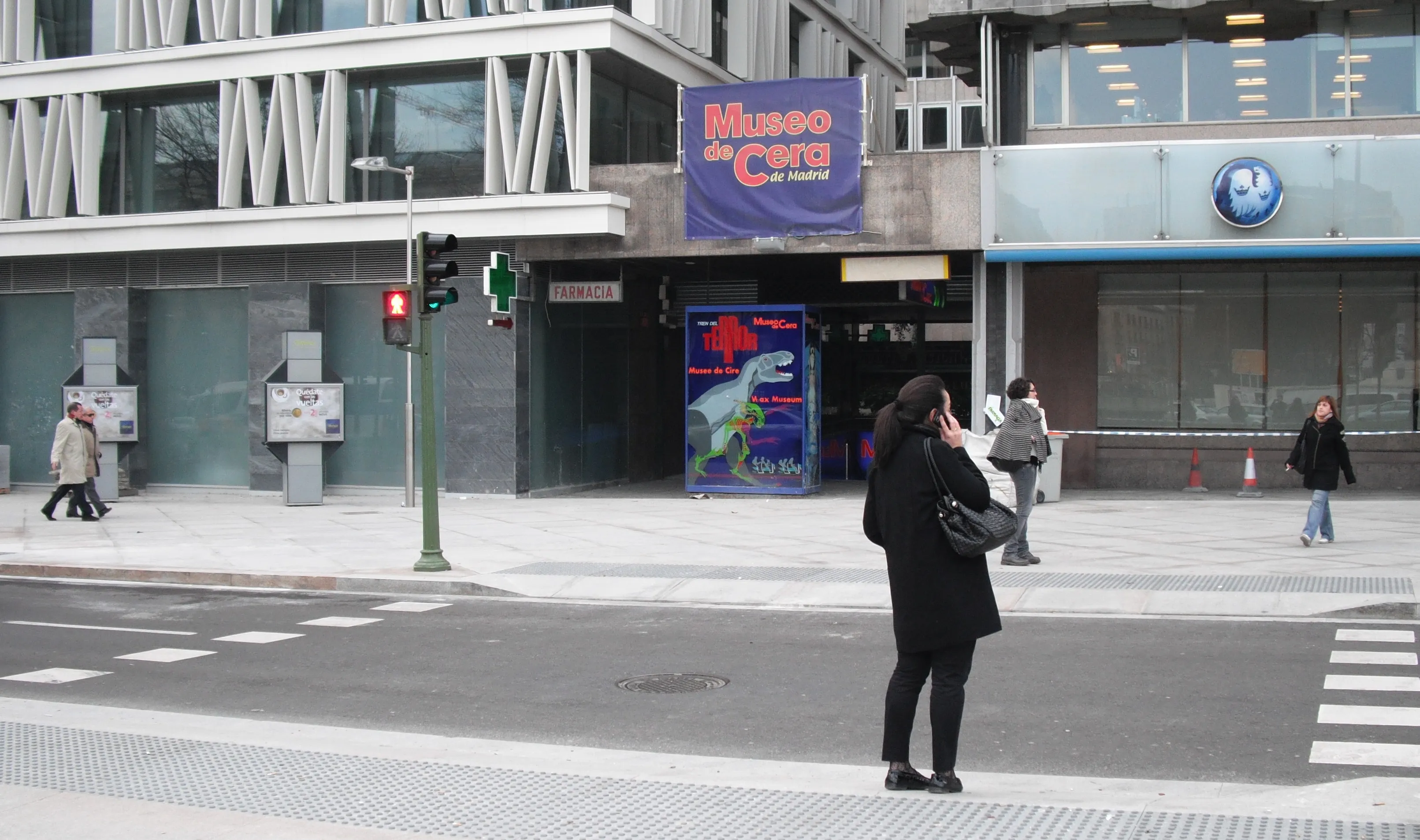 Exterior del Museo de Cera de Madrid con un cartel azul que dice 'Museo de Cera' sobre la entrada, gente caminando por la acera y la calle frente al edificio
