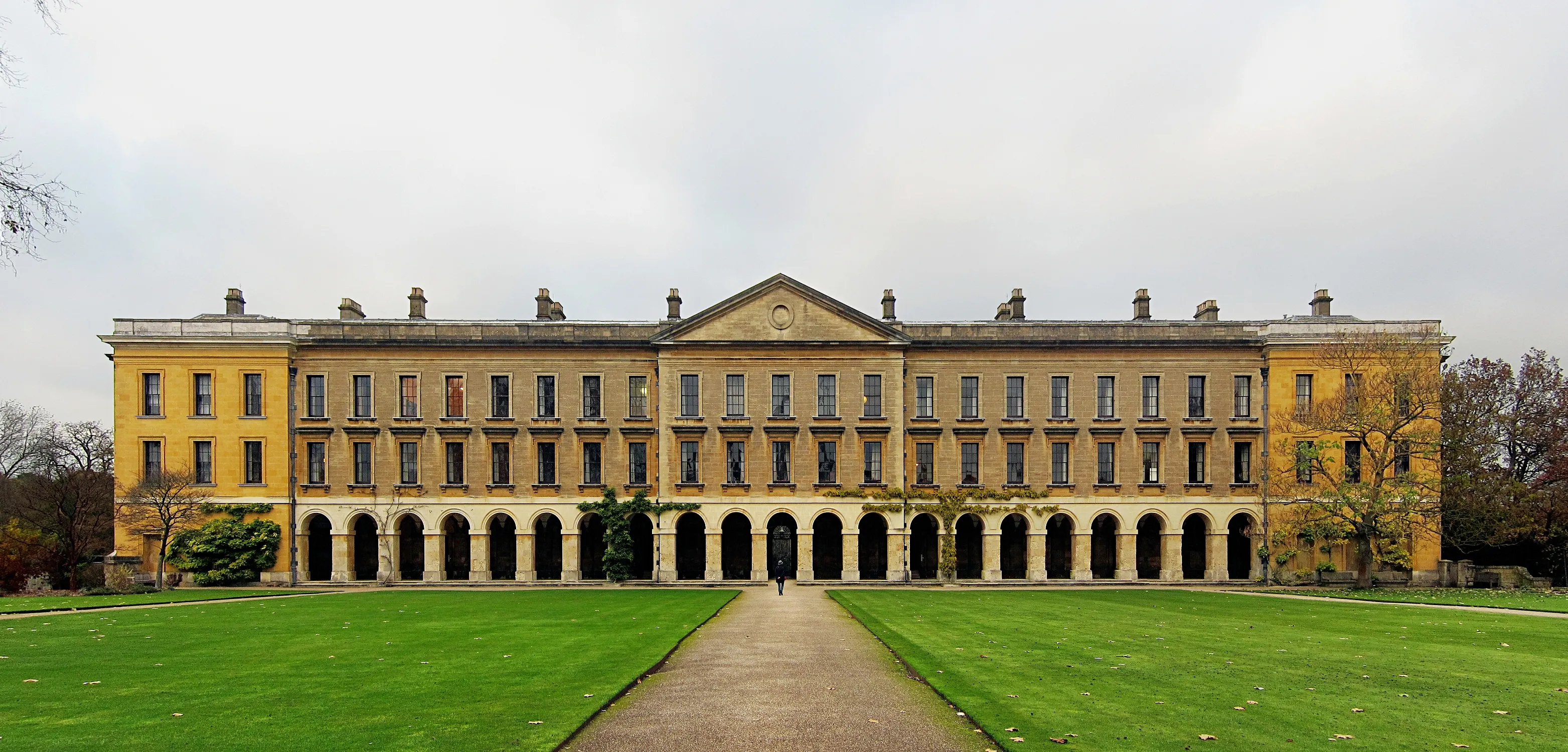 Wide exterior view of Magdalen College's New Building, a long classical stone facade with arched colonnade and green lawn with central path