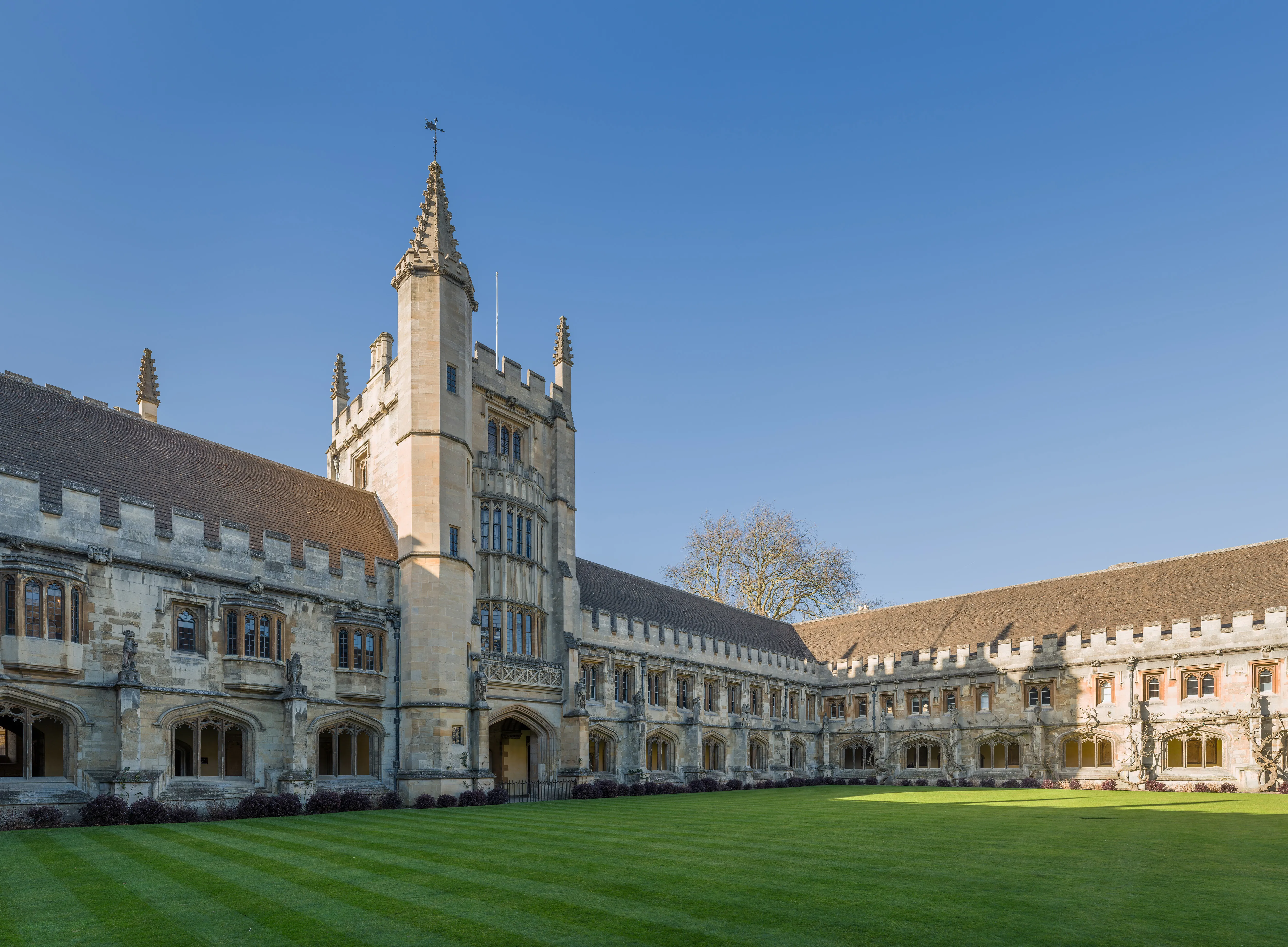 Founders Tower en de omliggende historische stenen gebouwen van de New Quad van Magdalen College onder een helderblauwe lucht, met een verzorgd groen gazon op de voorgrond.