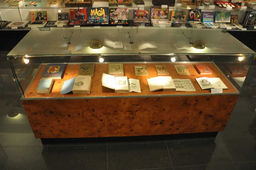 Glass display case with books and papers inside, illuminated by spotlights, in a museum setting