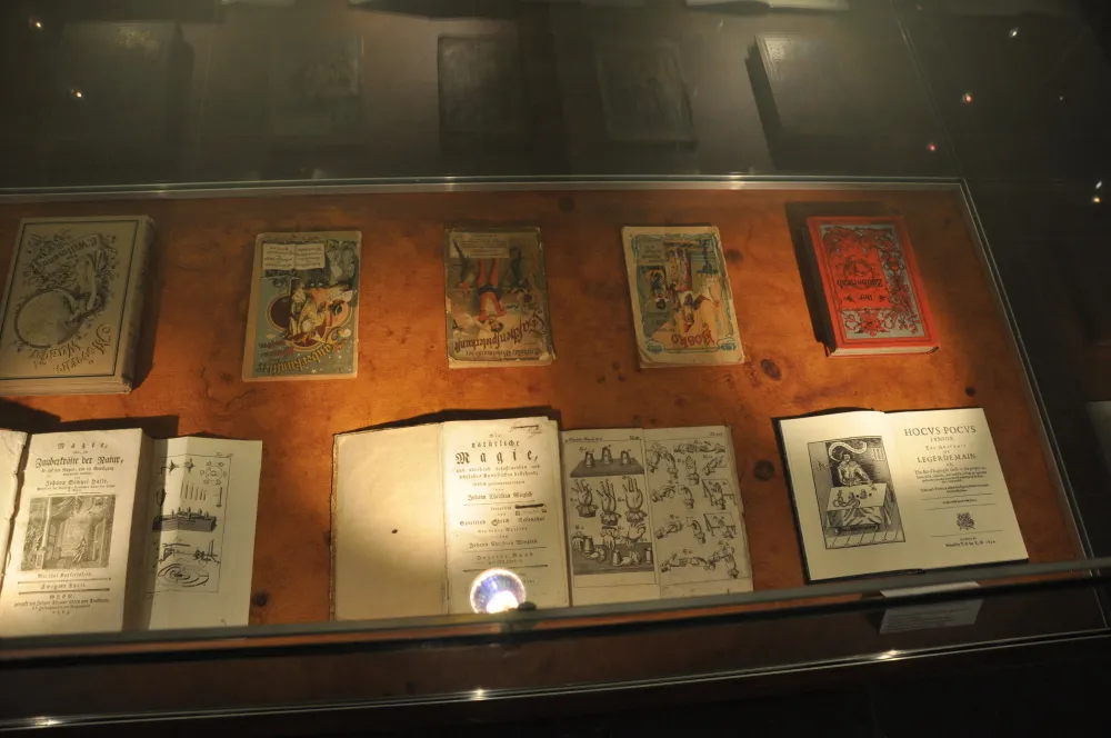 Vitrina de cristal que contiene libros de magia vintage y manuales ilustrados sobre un fondo de madera