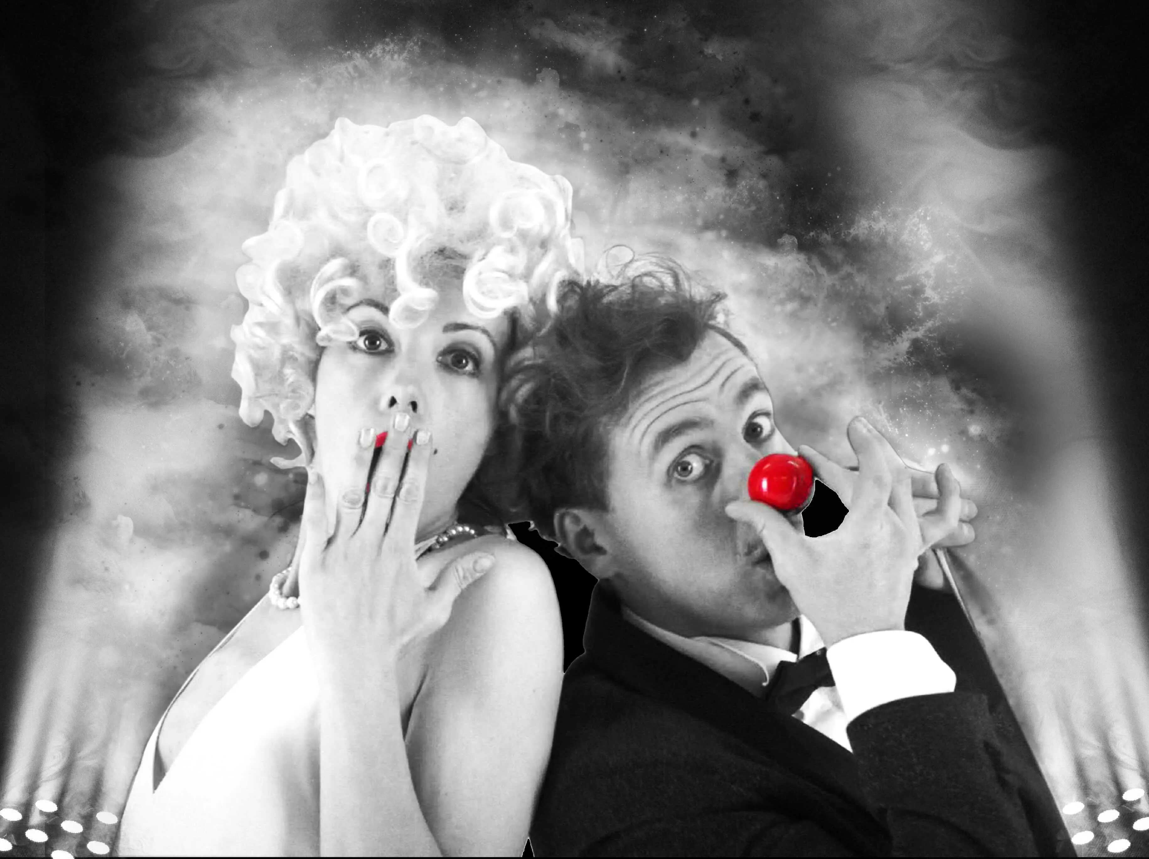 A man in a tuxedo with a red clown nose and a woman with a blonde wig, both making surprised expressions against a smoky background with stage lighting.