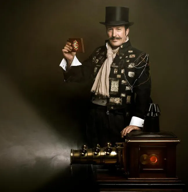 a magician in a top hat and decorative coat holding a glowing object next to a vintage machine