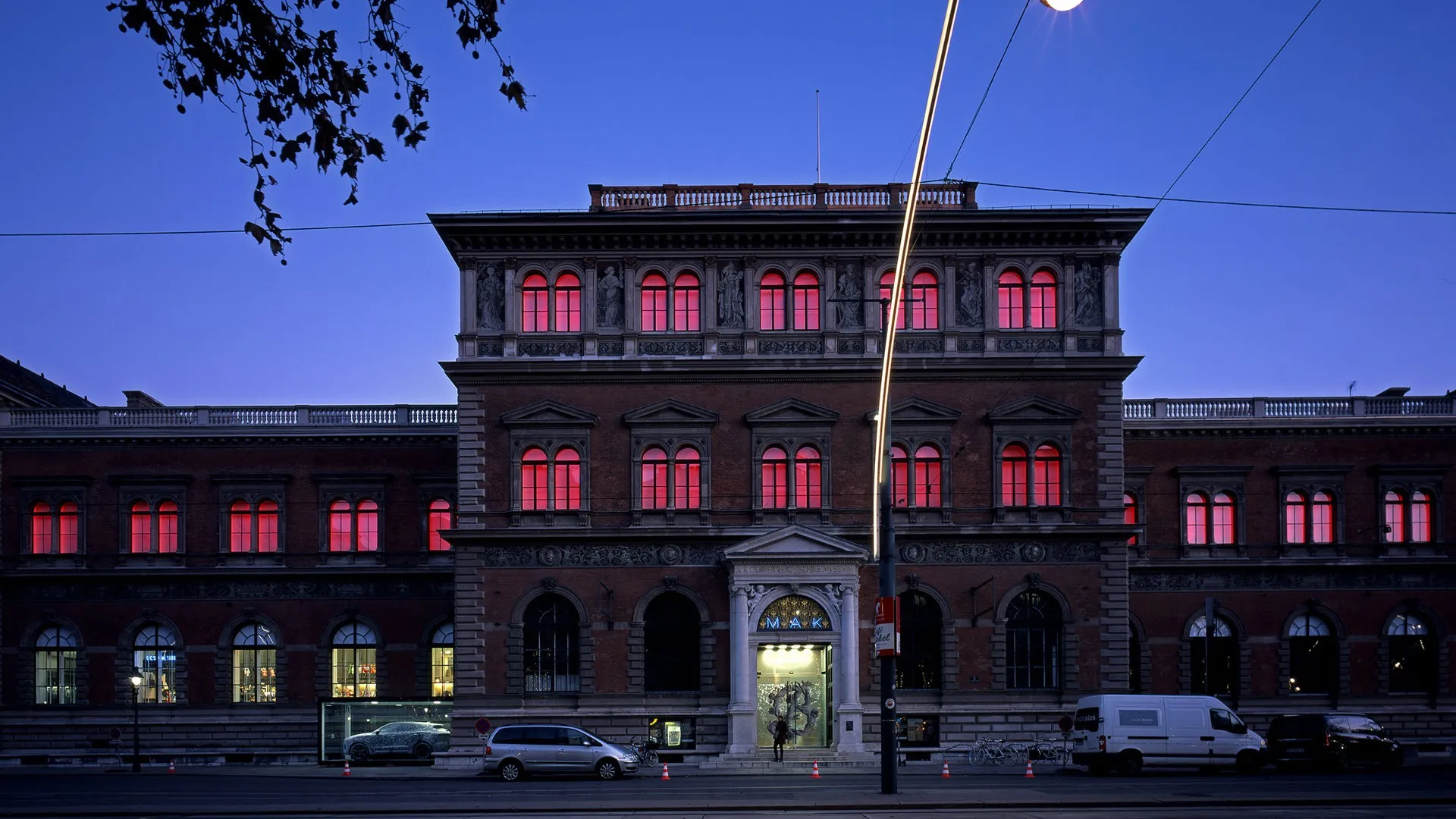 Het MAK - Museum voor Toegepaste Kunst gebouw bij schemering, met rood verlichte ramen en een blauwe lucht.