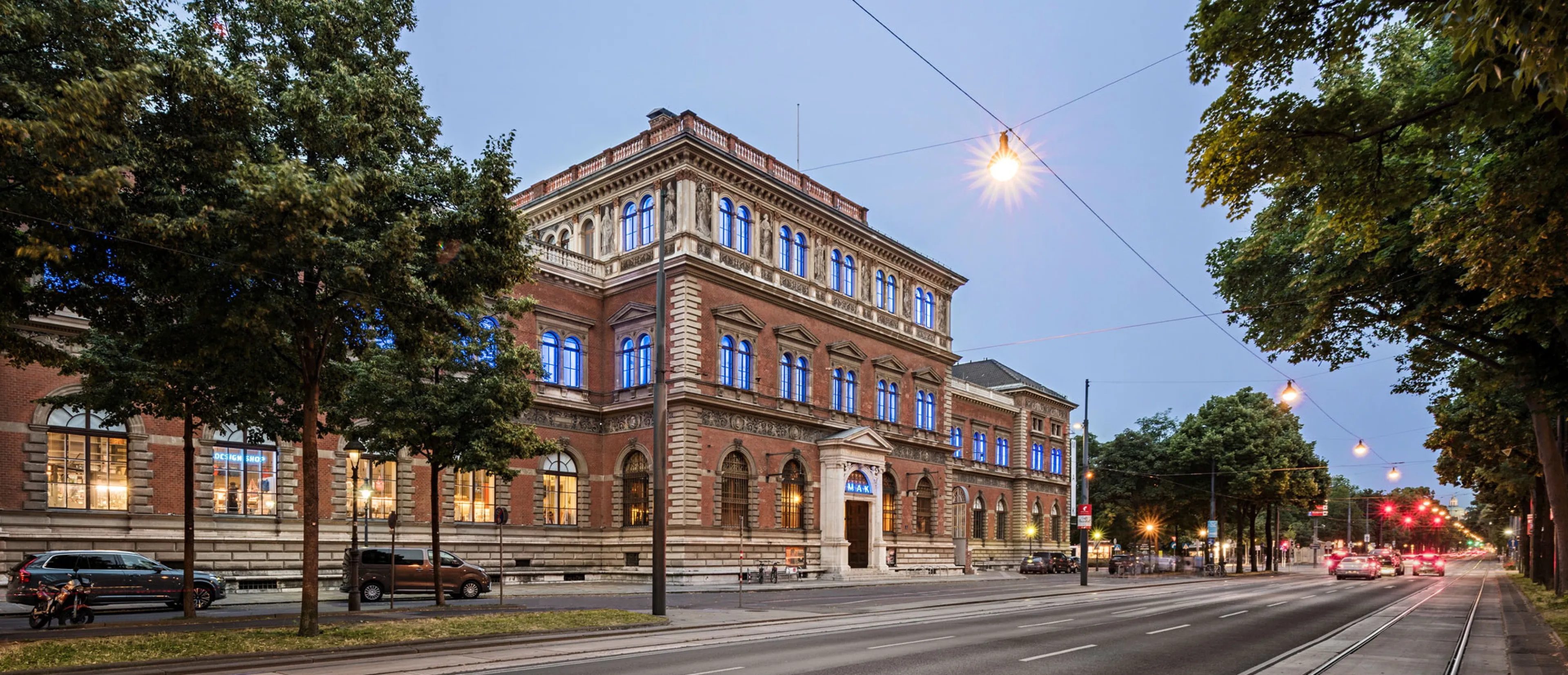 Het MAK - Museum voor Toegepaste Kunst gebouw bij schemering, een groot bakstenen gebouw met verlichte ramen, omringd door bomen en straatverlichting.