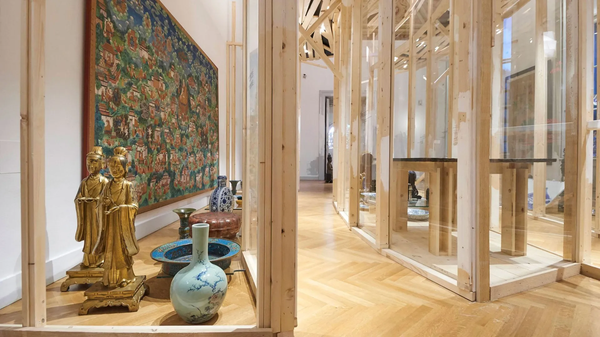 Tentoonstellingsgalerie met een groot wandtapijt, gouden beeldjes en een keramische vaas in vitrines