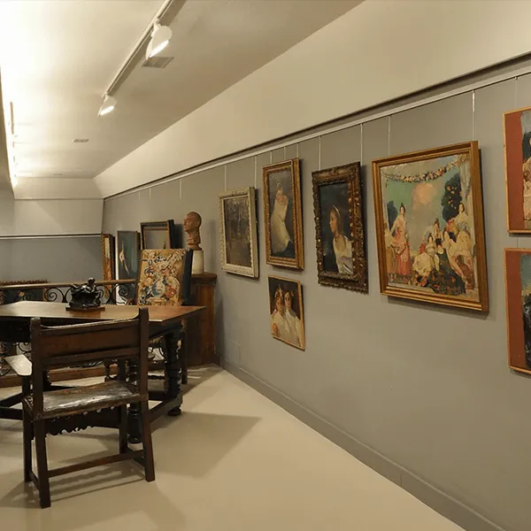 Gallery room with paintings on gray walls, wooden table and chairs in the foreground