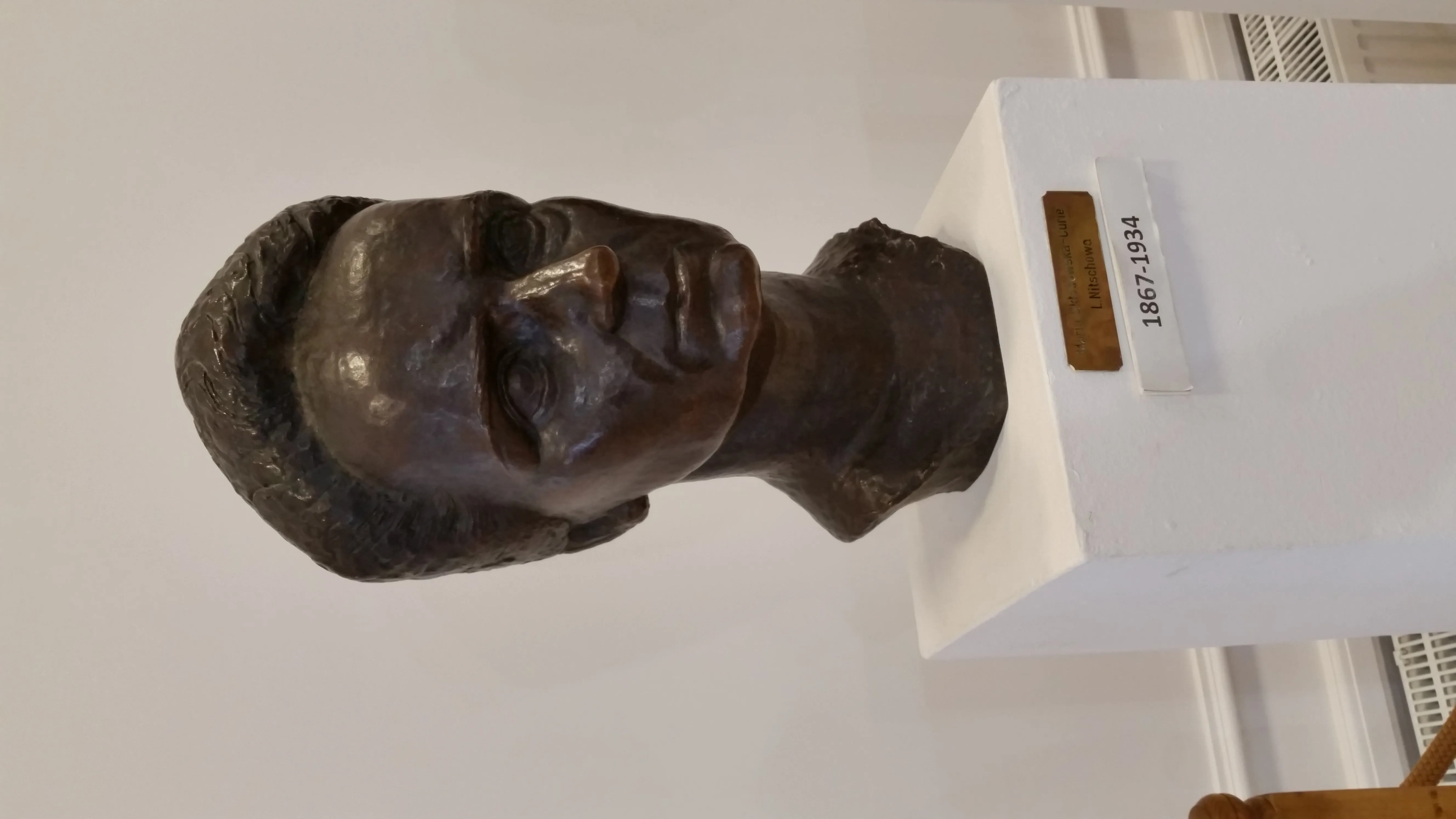 bronze bust of a woman on a white pedestal with a label