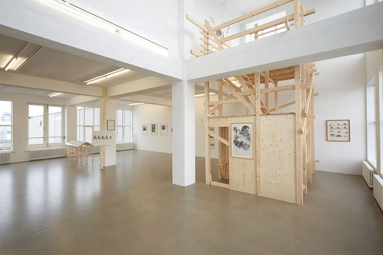 Jasne wnętrze galerii w Marshall House z białymi ścianami, dużymi oknami, polerowaną podłogą oraz dużą, wielopoziomową drewnianą konstrukcją instalacyjną w środkowej prawej części pomieszczenia.