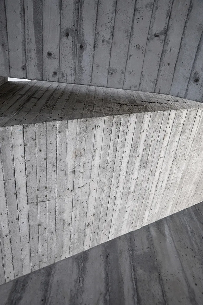 Zbliżenie na powierzchnię betonu architektonicznego z widoczną teksturą słojów drewna i śladami po sękach na zakrzywionym elemencie konstrukcyjnym