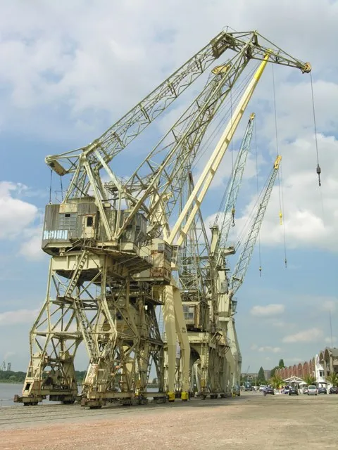 Grandes grúas portuarias industriales sobre un muelle pavimentado a lo largo de la costa de Amberes bajo un cielo parcialmente nublado