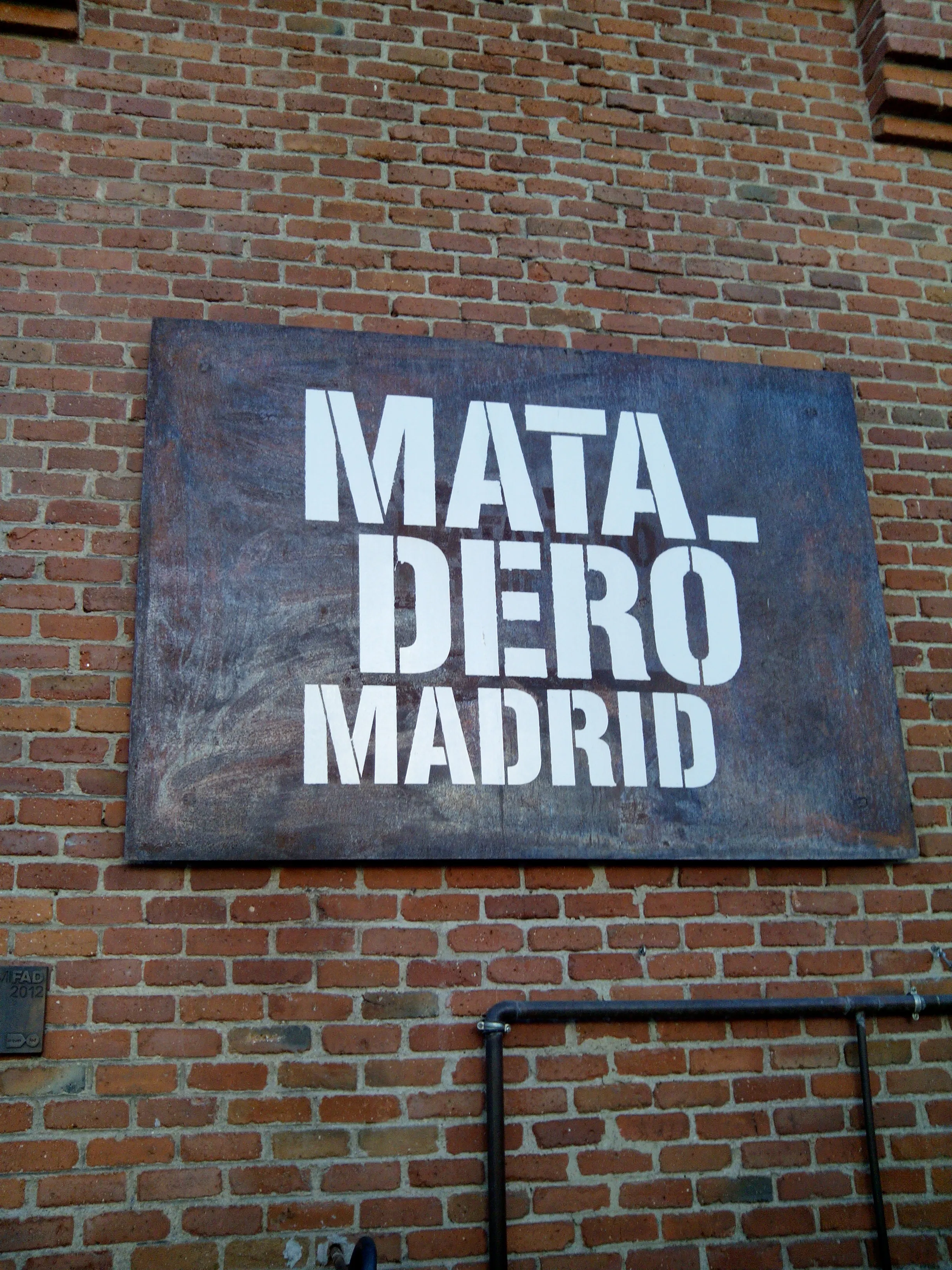 A metal sign with 'MATA- DERO MADRID' in white letters on a dark background, mounted on a red brick wall