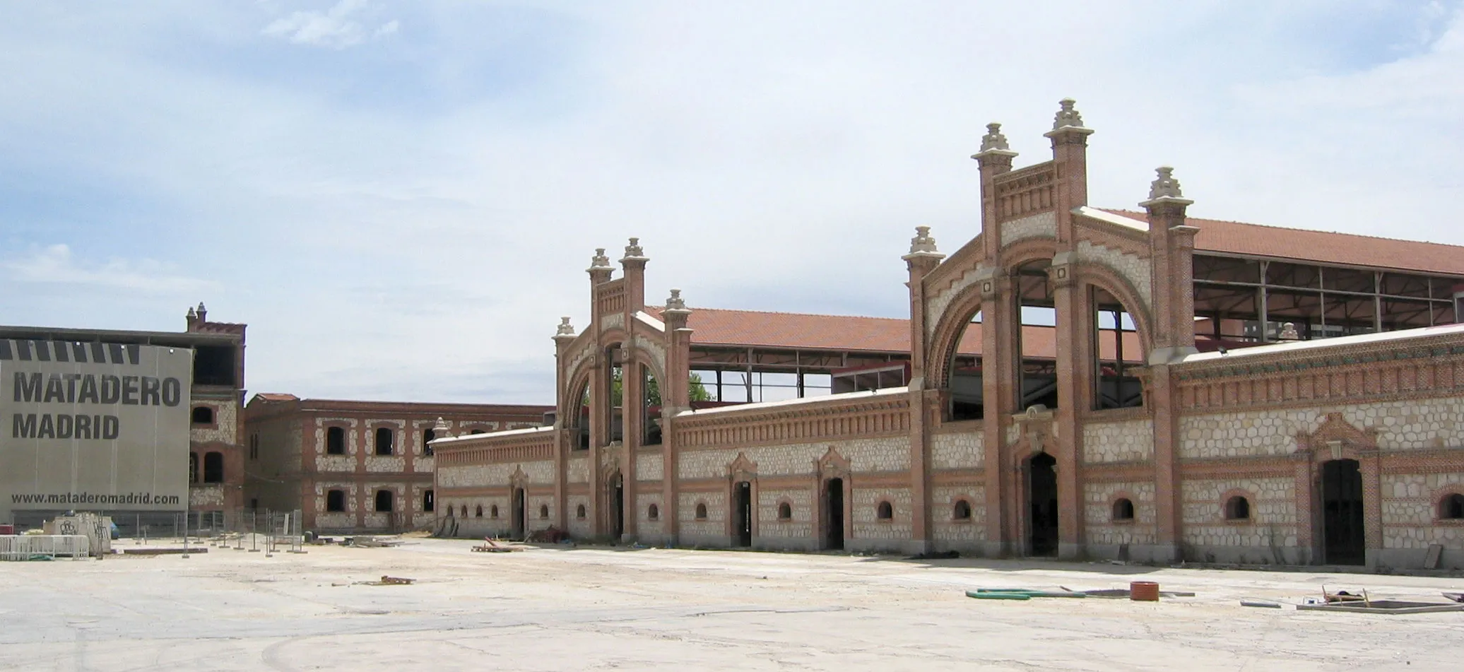 Kompleks Matadero Madrid z ceglanymi budynkami, łukowatymi wejściami i dużym otwartym dziedzińcem pod błękitnym niebem