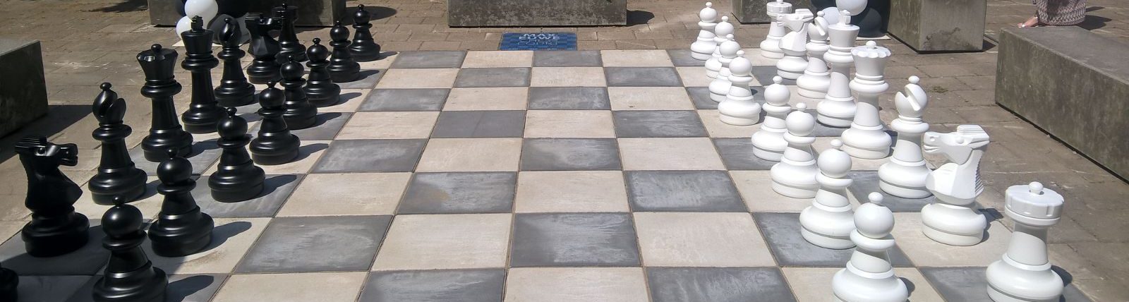 Giant outdoor chessboard with black and white pieces arranged on a paved plaza