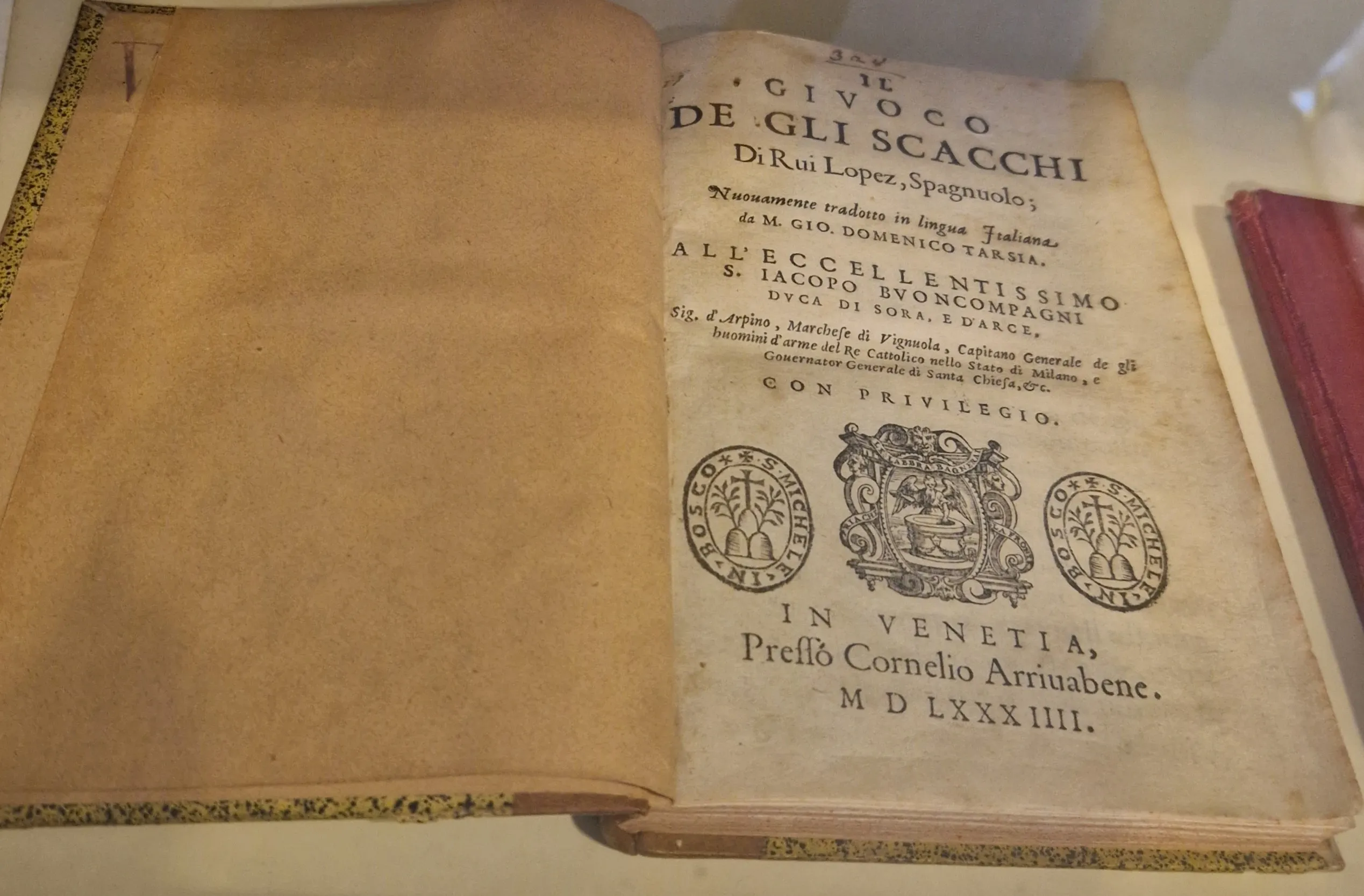 An open antique book with the title 'Il Cibo de gli Scacchi' and text in Italian, showing two circular seals and a central crest on the page.
