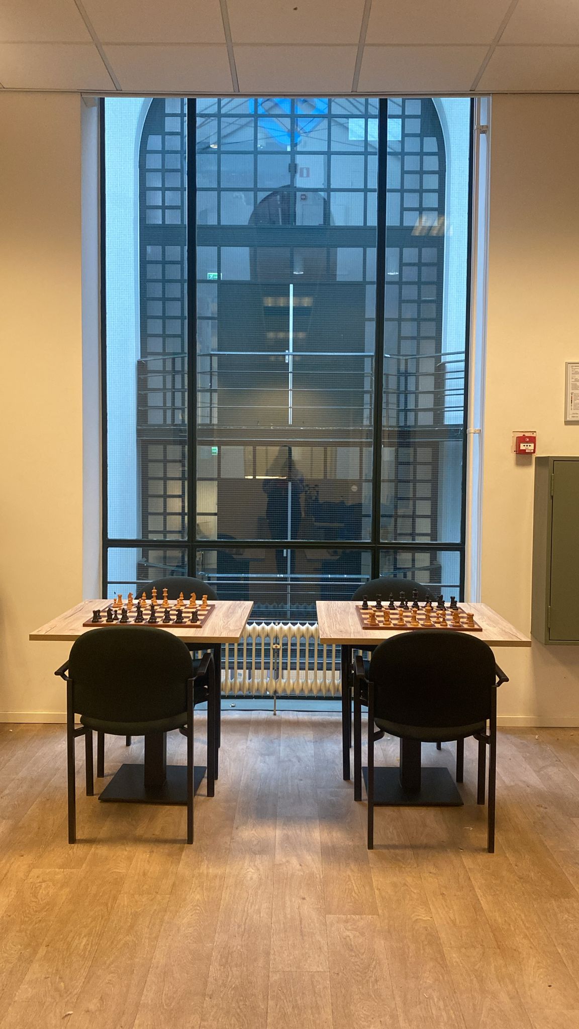 Two chessboards set up on tables in a museum space with large windows, showcasing exhibition displays at Max Euwe Centrum