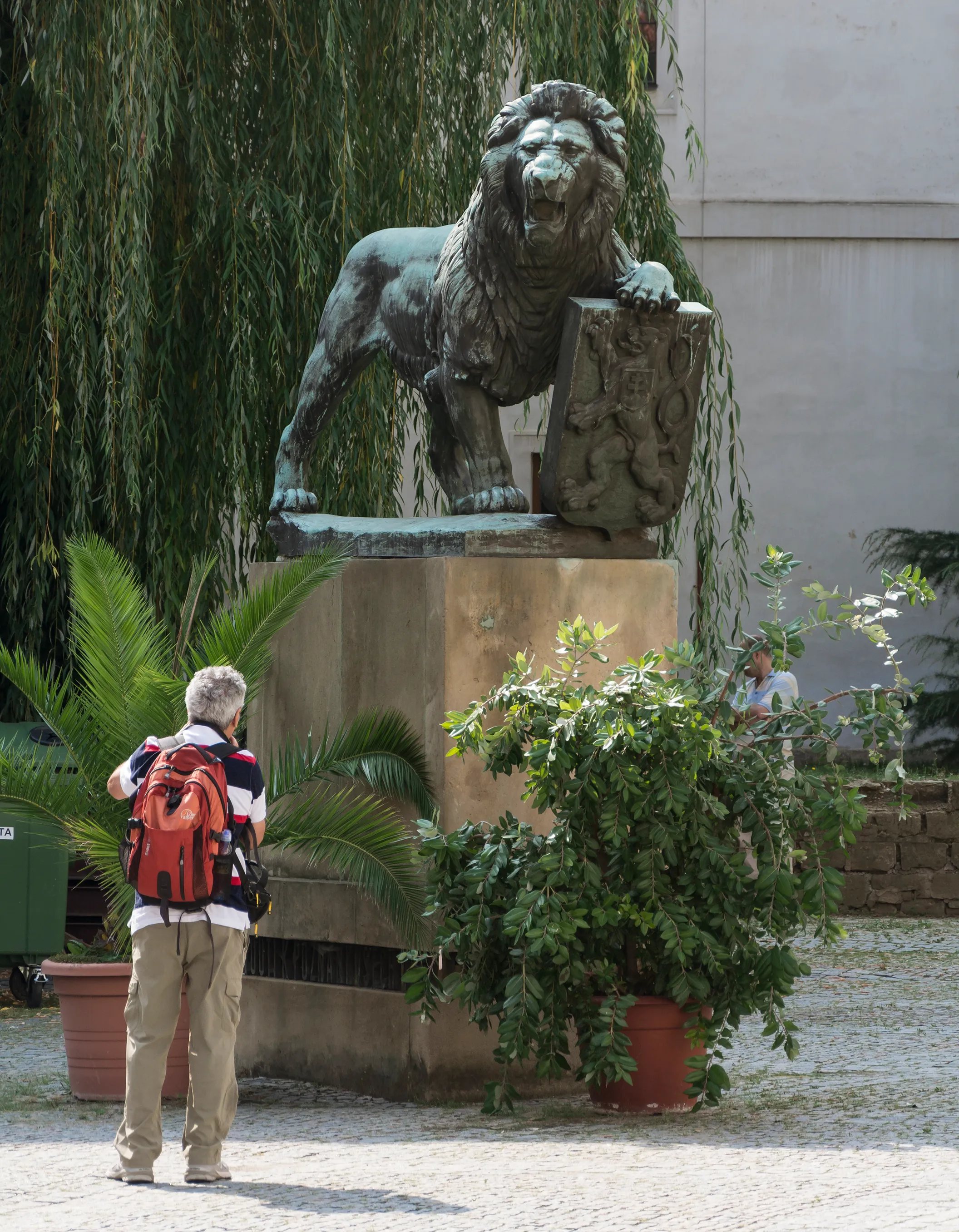 Bronze lion statue on a pedestal in a courtyard with a person observing it