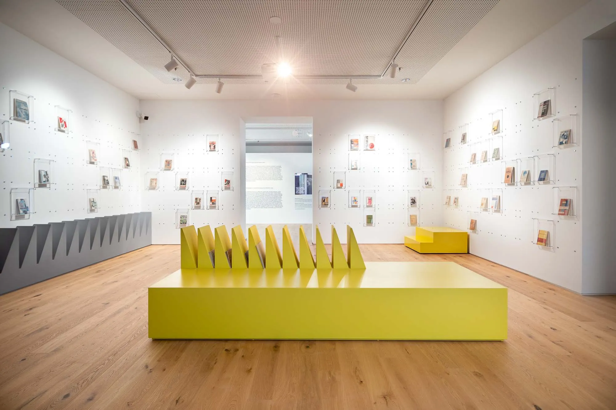 Una galería con paredes blancas que exhiben obras de arte enmarcadas, una escultura amarilla en el centro y suelos de madera